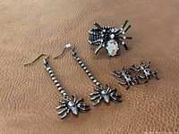Photo showing set of spider and ant themed jewelry on brown surface, including dangle spider earrings, spider stretch ring, and ant stud earrings