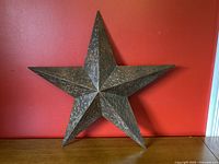 Front view of five-pointed embossed bronzed metal wall star against red background on wooden surface.