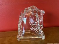 Front view of clear glass horse head sculpture against red background, highlighting detailed mane and facial features.
