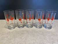Five clear Collins cocktail glasses with red stylized flamingo bird designs and 24K gold detailing, displayed on a flat surface.