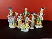 Five colorful porcelain figurines on a dark surface with red background, showing front details.