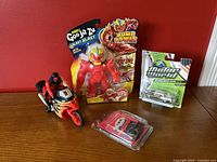 Photo showing all items: poseable motorcycle with rider, Goo Jit Zu Galaxy Blast in package, loose red Air Vac Blazagon figure, and 1955 Chevrolet Bel Air Motor World American diecast car in sealed packaging.