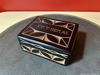 Top angled view of rectangular dark stained wooden trinket box with light carved geometric designs and 'ST. THOMAS' inscription on lid.