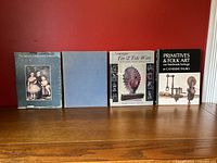 Four hardcover reference books standing on a wooden surface against a red background. Titles visible include The Ontario Community Collects, Antique Tin & Tole Ware, and Primitives & Folk Art. One book has a blue cover without a visible title.