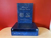 Front view of one book volume standing on top of slipcase for second volume, all set against a red wall background.