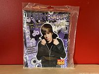 Front view of sealed Justin Bieber 2011 exclusive sticker album featuring image of Justin Bieber in black jacket on purple background with graphics.