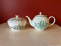 Photo showing porcelain teapot and serving bowl side by side on a table with red background.