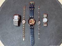 Top-down view of all five ladies wrist watches laid flat on dark textured surface showing variety of styles, bands, and faces