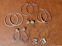 Six pairs of earrings displayed on brown surface showing variety of styles including hoops and dangles.