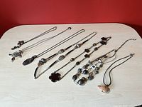 Photo showing all seven eclectic necklaces laid out on a light surface against a red background, capturing full variety of styles and materials from floral pendants to fish charm and multi-strand beads.
