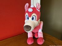 Front view of the Mega Man Rush robot dog plush toy, showing the full body with details of the face, ears, and front legs against a red background.