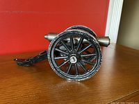Side view of the miniature 1862 Napoleon 12-pounder field cannon displayed on wooden surface with red background.