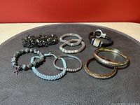 Photo showing 9 mixed bracelets on a dark surface, featuring a variety of designs including beaded, leather, chain, and bangles.