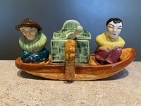 Front view of complete salt and pepper set on boat base with Asian couple figures and green basket cruet.
