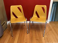 Pair of vintage yellow molded plastic chairs with chrome legs against a red wall on hardwood floor, showing front and side views.