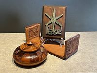 Hand stitched leather book holder with floral embossing on sides, carved wooden bowl with lid, and brass Peace plaque on wood displayed upright with metal stand