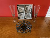Full set showing two tall champagne glasses, a boxed set of four decorative glass dishes with card suit designs, and a black wrought iron candle holder shaped like a clock face.