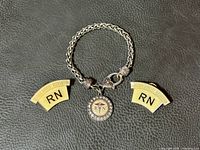 Full view showing silver tone woven link bracelet with circular RN charm featuring rhinestone border and copper tone accents between two bright gold tone RN pins issued by Ontario Nurses Association.