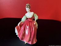 Porcelain figurine showing woman in red dress with green sleeves standing posed against red background
