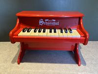 Front view of red wooden Schoenhut toy piano showing 25 black and white keys and wooden stand base.
