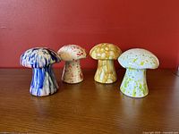 Front view of four ceramic mushroom shakers on wooden surface against red wall