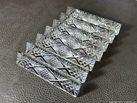 Seven crystal utensil rests arranged in a row showing detailed cut glass patterns and starbursts.