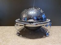 Front angled view of the vintage silver plated caviar dish showing ornate engraved domed lid, raised on four claw feet with the inner bowl inside the outer ice container.