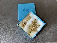 Set of gold-tone clip-on earrings and matching floral brooch pin with rhinestone accents inside a blue Simpson jewelry box on white cushioned interior.