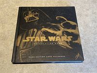 Front cover of the hardcover Star Wars RPG Saga Edition Core Rulebook showing black cover with gold embossed logo and artwork of Darth Vader and a droid.