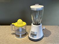 Oster 8-speed blender and Starfrit electric citrus juicer side by side on a surface.