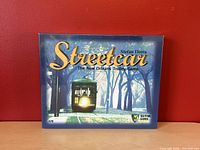 Front view of the boxed game featuring a trolley headlight on a street at night with title and author visible.