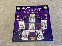 Front cover of paperback Tarot Coloring Book showing six tarot card illustrations and mystical iconography on purple background.