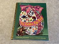 Front cover of The Golden Egg Book showing colorful floral egg and rabbit illustration with green background and gold patterned spine