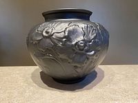 Front angled view showing the embossed poppy floral details and round shape.