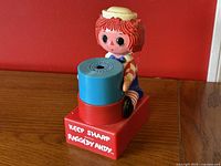 Front close-up view of the Raggedy Andy pencil sharpener featuring the red base with white text and the character on top with a blue and red sharpener cylinder.