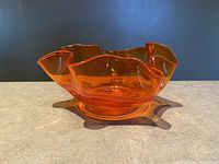 Front view of the vintage amberina orange ruffled edge art glass bowl on a neutral surface with a dark background.
