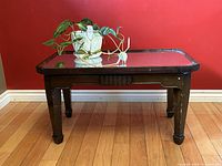 Front view of vintage Art Deco coffee table with beveled mirror top, carved wooden legs and apron detail on hardwood floor against a red wall.