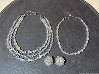 Full set laid out including the three-strand necklace, single-strand necklace, and pair of clip-on earrings on a black surface.