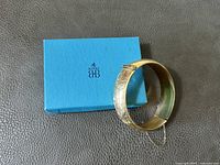 Vintage Birks hinged bangle bracelet placed next to its light blue box with Birks logo on top, showing full bracelet with safety chain.