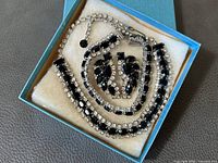 Top-down view of necklace, bracelet and earrings arranged in blue presentation box lined with cream felt