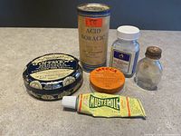 Overview of six vintage medical and medicinal collectible containers including bottles, tins, and cream tube.
