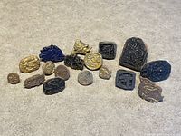 Photo showing entire collection of 16 vintage clay textile stamps laid out on a flat surface, varying in size, shape, and color.