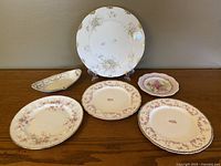Photo showing six porcelain plates and one serving dish with floral and gold accented designs