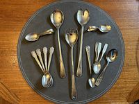14-piece set arranged on brown leather placemat showing all spoons and serving utensils