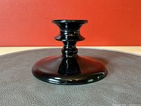 Front view of black glass candlestick on dark surface against red wall