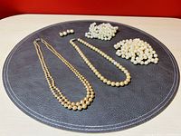 Four faux pearl necklaces and one pair of clip-on earrings displayed on a dark surface with visible varied bead sizes and design details.