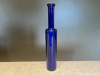 Tall slender vintage cobalt blue glass bottle shown from the front against a neutral background to highlight true color and shape.