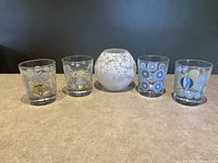 Full lot showing the white frosted cherry blossom glass globe lamp and four decorated glass tumblers with unique colorful designs including mushrooms and animals.