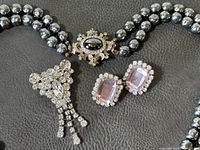 Close-up of necklace clasp, brooch, and earrings showing materials and design detail.