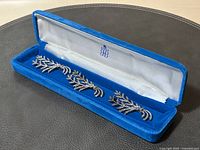 Three marcasite leaf branch brooches in a blue velvet Birks box with white satin lining, arranged side by side showing detailed stones and silver work.